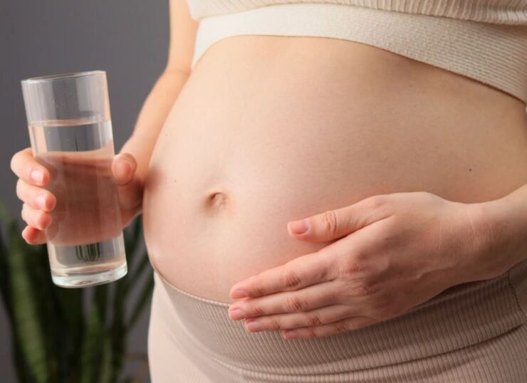 prikaz trudnice u sportskoj odeći koja u ruci drži čašu vode