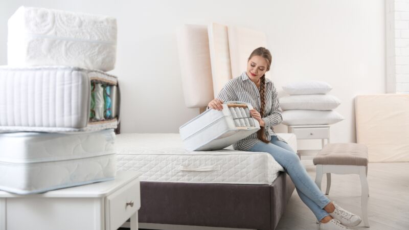 Osoba sedi na krevetu i pokazuje unutrašnju strukturu dušeka sa slojevima