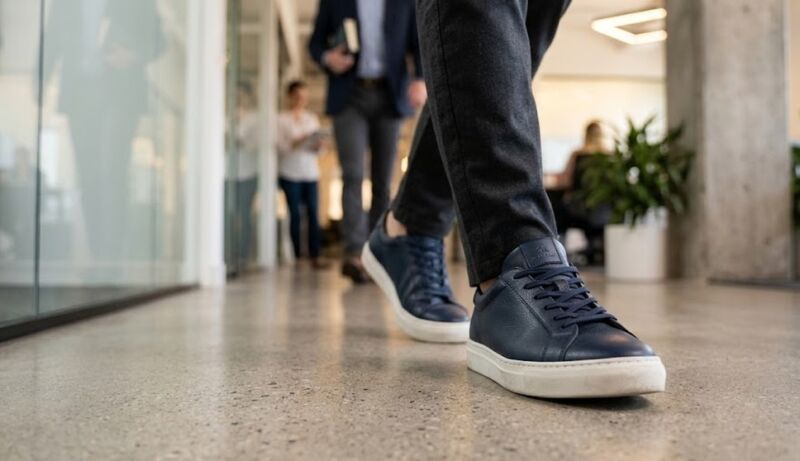 Muškarac u poslovnim pantalonama i elegantnim teget patikama šeta kroz kancelarijski prostor
