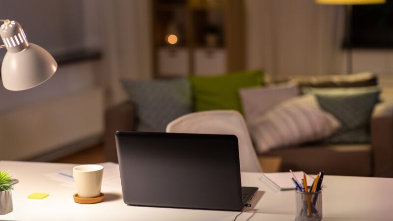 Laptop i šolja kafe na radnom stolu uz upaljenu lampu.